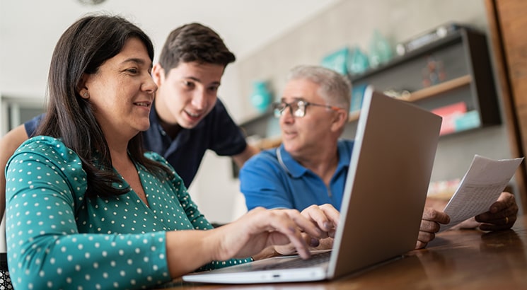A couple sitting at their dining room table, the woman is typing on a laptop while their son looks on